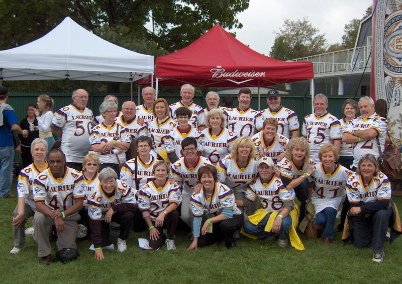 A group posed near a football field wearing white, purple and yellow jerseys.
